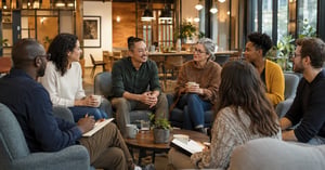 A diverse group of adults chat, drink coffee, and take notes during a relaxed community meetup in a modern venue.