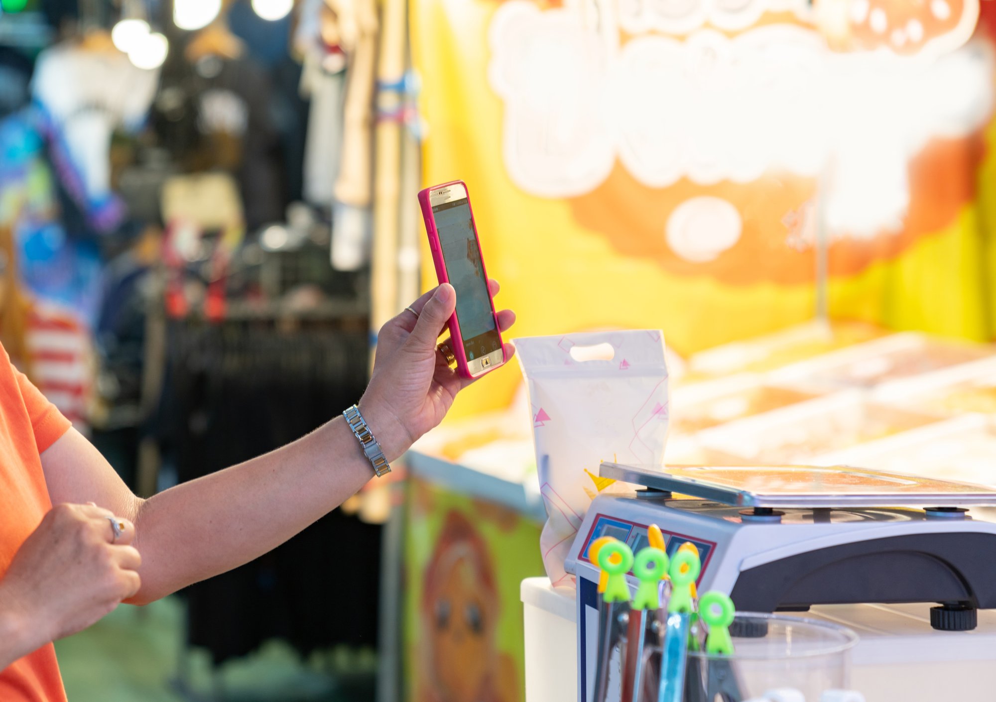 Person med smartphone til mobilbetaling ved en farverig gademarkedsbod med merchandise. Person med smartphone til mobilbetaling ved en farverig gademarkedsbod med merchandise.